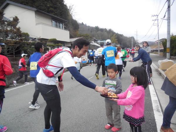 沿道に小さな男の子と女の子がお盆にお菓子を乗せて持っていて、男性のランナーがお盆からお菓子をもらっている写真